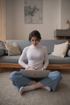 A woman sits cross-legged on the floor using a laptop, showcasing modern remote work lifestyle.