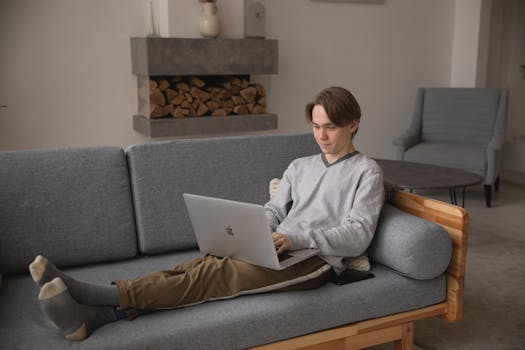 A young man comfortably working on a laptop at home, symbolizing modern remote work and technology.