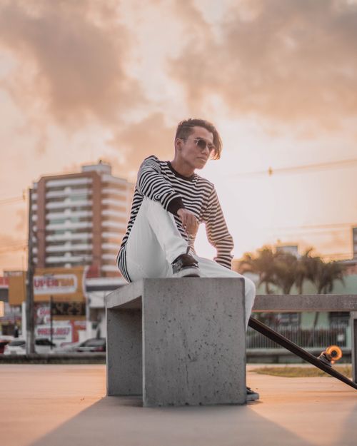 Free Fashionable young man sitting on a bench with a skateboard, enjoying a sunset in the city. Stock Photo