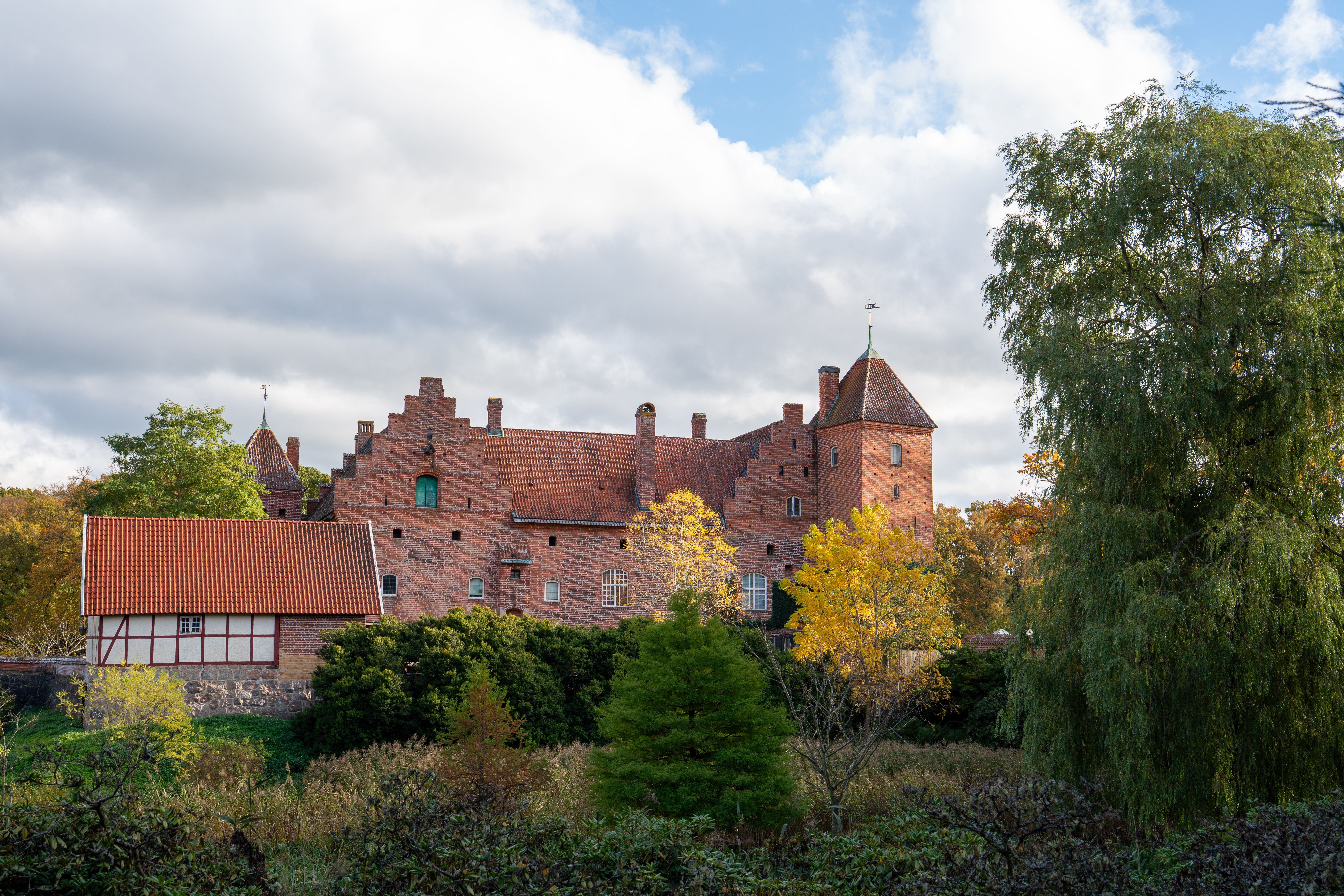 Charming brick castle in Sweden surrounded by vibrant autumn foliage under a cloudy sky.
