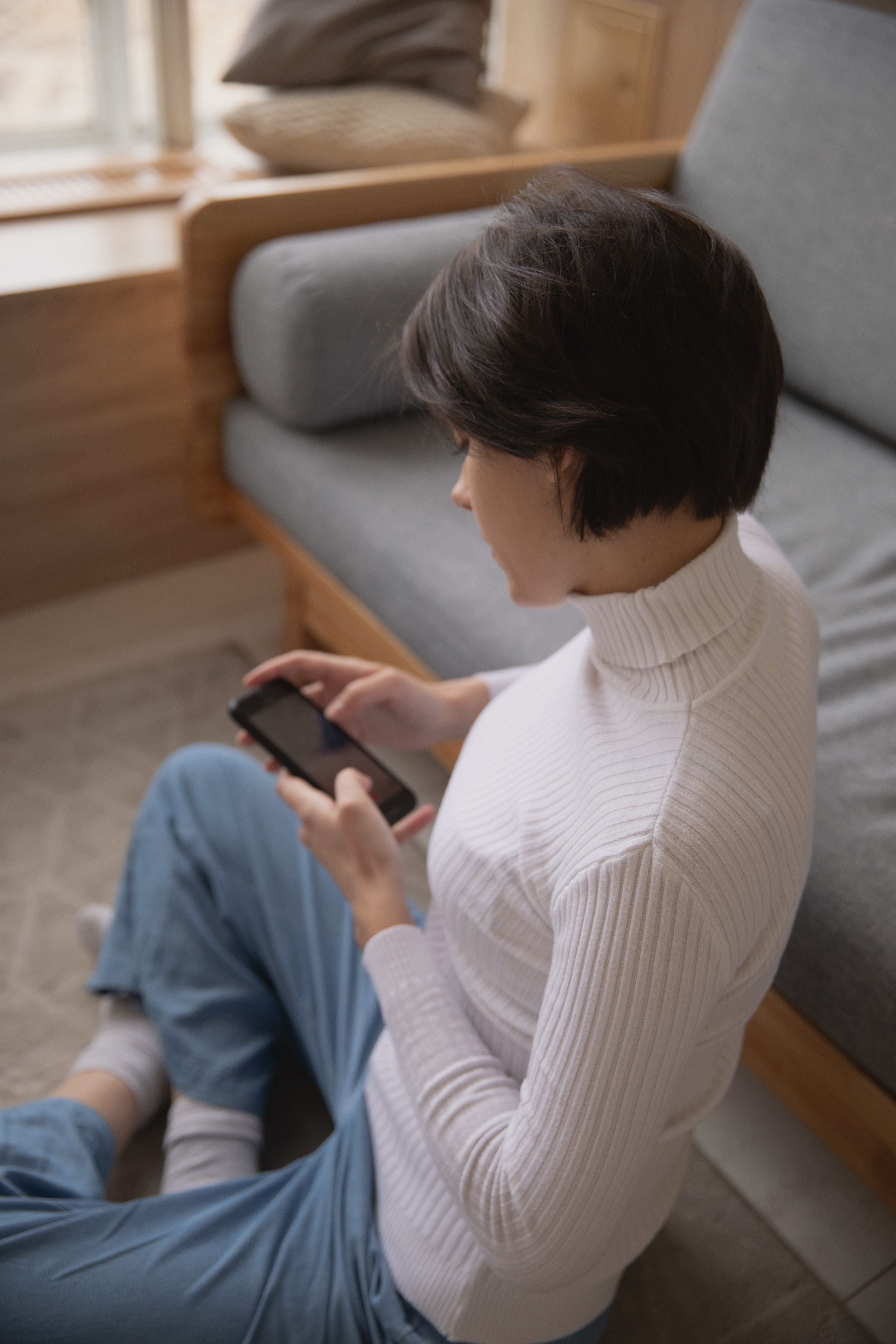 一位年轻女子穿着休闲服装，在室内舒适地坐着，正使用智能手机