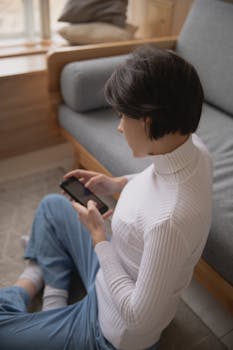 Young woman in casual outfit using smartphone while sitting comfortably indoors.