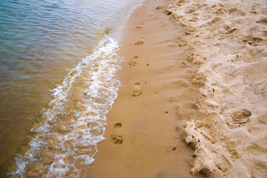 Serene beach scene with footprints in the sand alongside gentle shore waves.