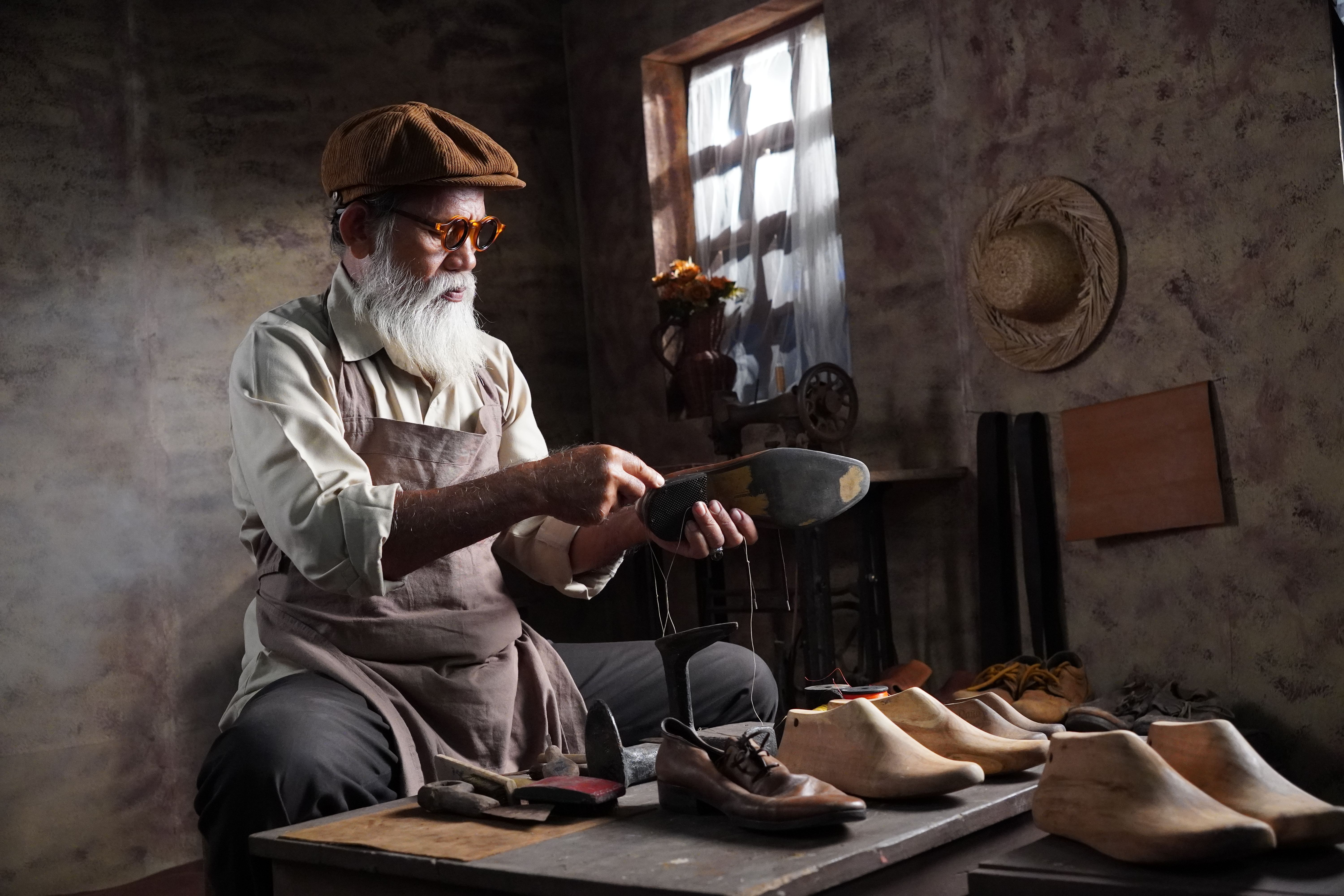 Elderly cobbler handcrafting leather shoes in a vintage workshop setting.