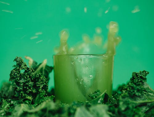 Bright vitamin juice near lettuce leaves on green background