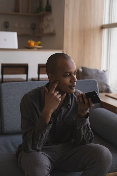 Pensive young ethnic man using smartphone at home