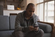 一个男人舒适地坐在光线充足的家中，专心使用着智能手机