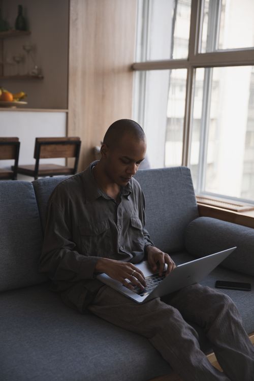 Free A man focuses intently on his laptop while sitting on a comfortable couch, epitomizing remote work lifestyle. Stock Photo