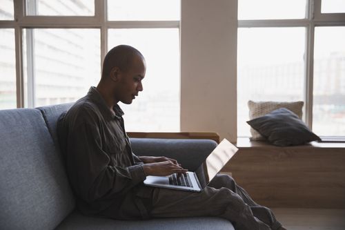 Free A man focuses intently on his laptop as he works remotely from a modern room with large windows. Stock Photo