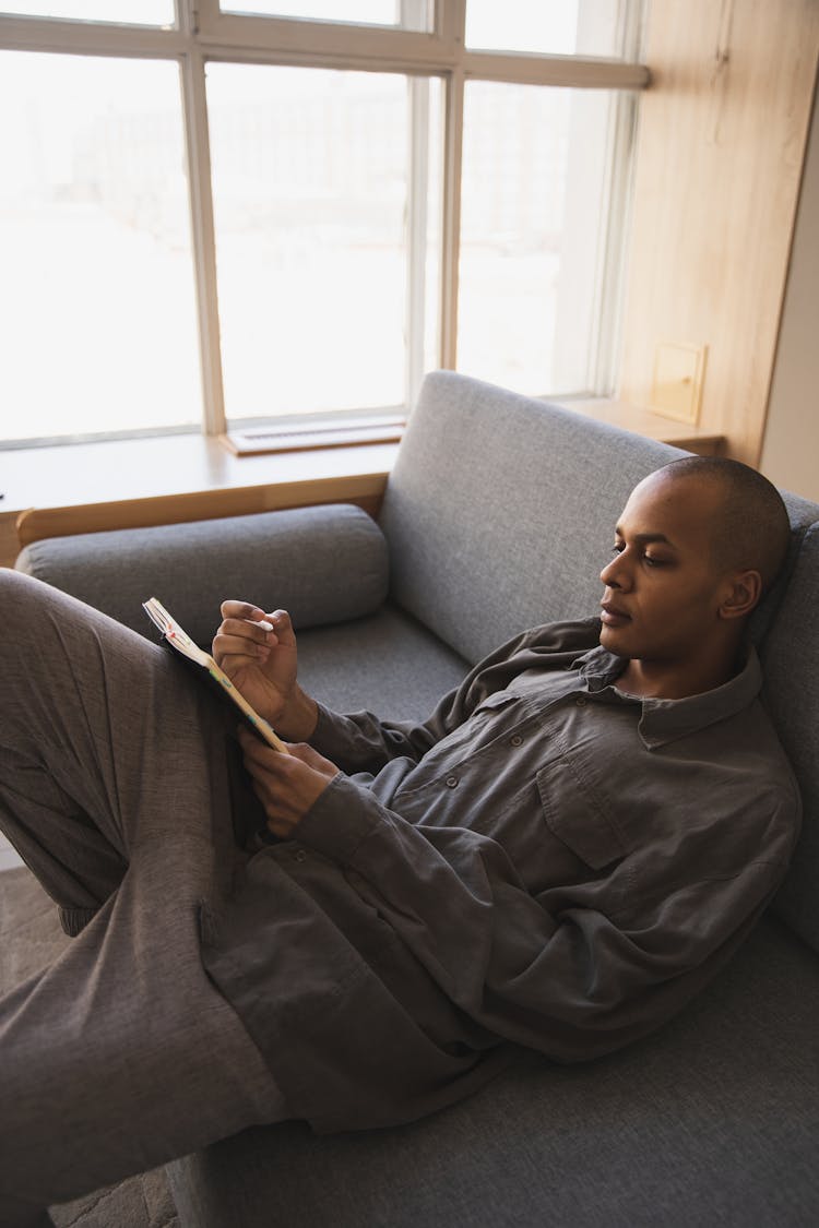 Focused Young Ethnic Man Lying On Couch In Living Room