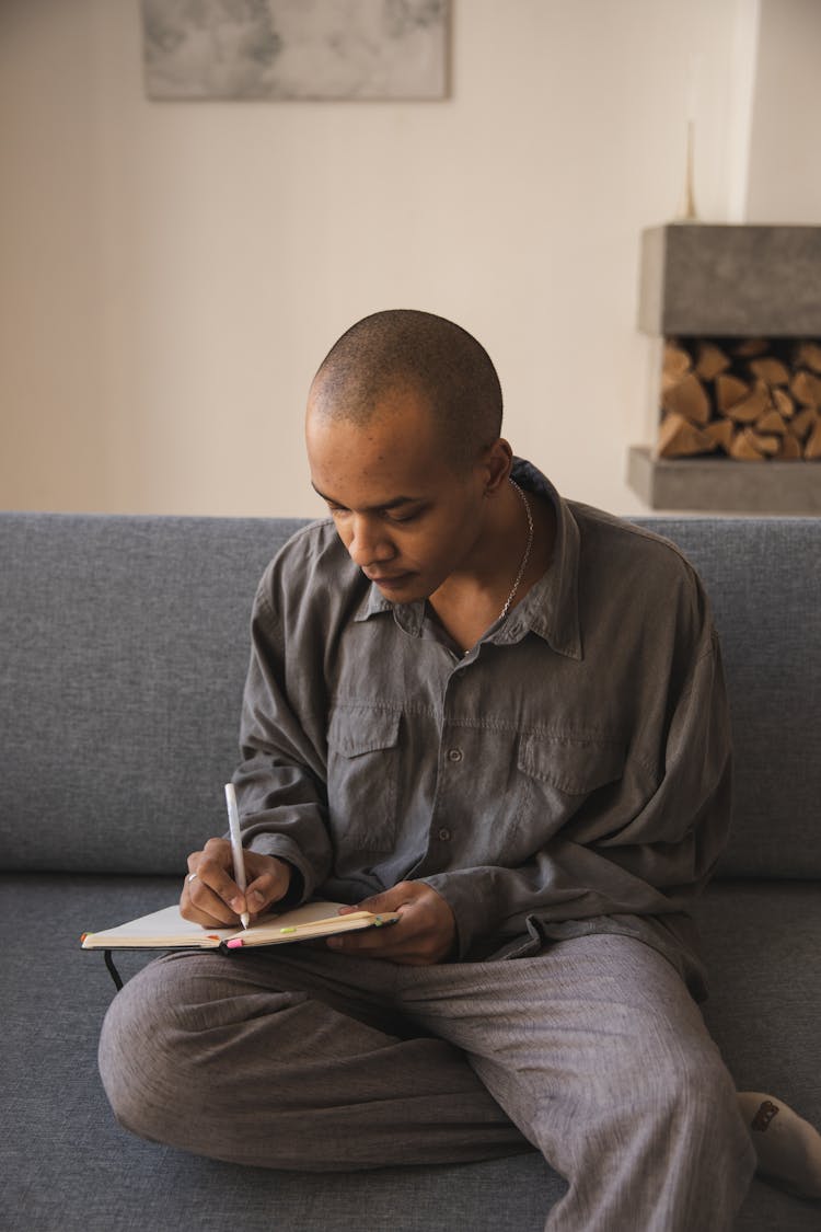 Thoughtful Young Ethnic Man Writing On Notebook At Home