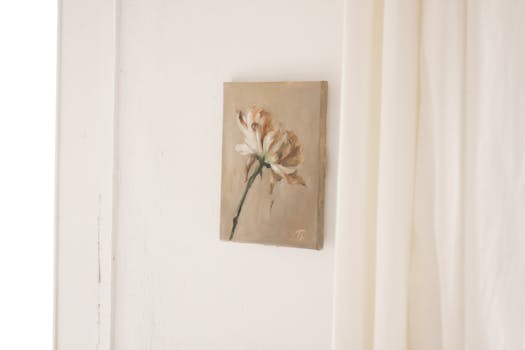 Picture of flower composition on beige canvas hanging on white wall near curtain