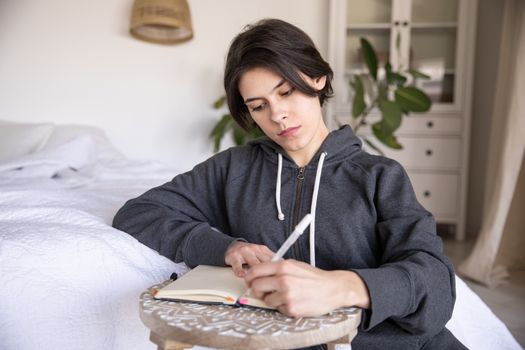 Young woman in a hoodie writing in a notebook at home, capturing a reflective moment.