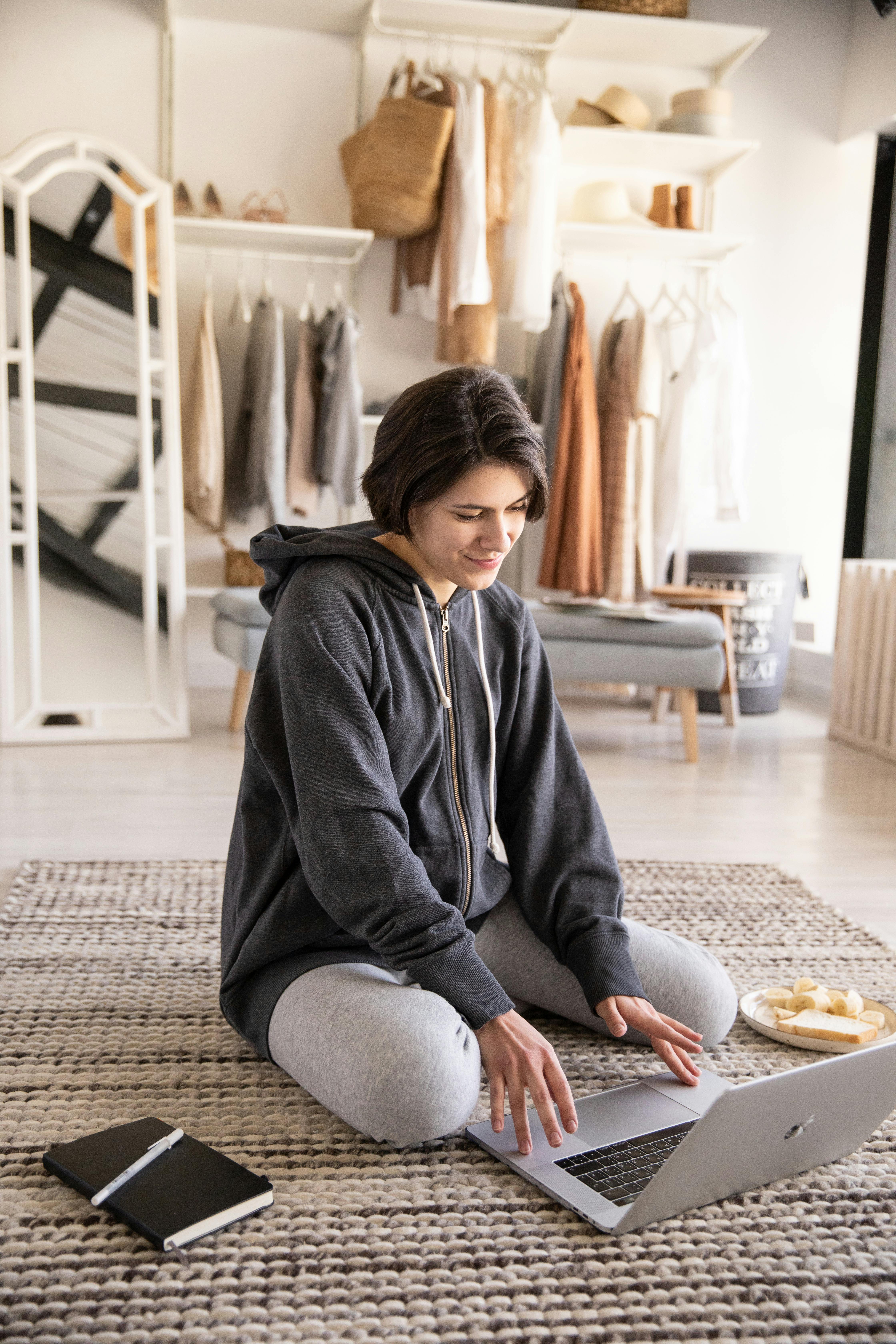 positive young woman using laptop on floor in living room