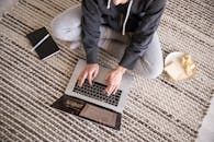 一名穿着休闲装的女子正用笔记本电脑远程工作，旁边放着另一台笔记本电脑和一些零食