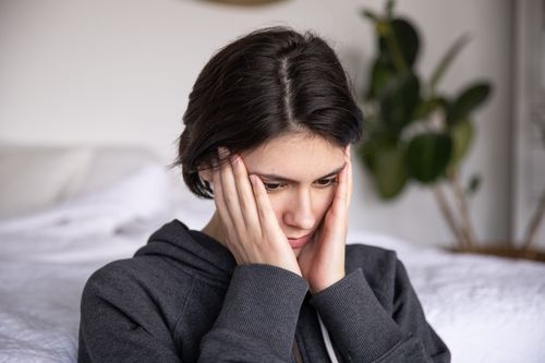 Free Woman sitting indoors in thought, wearing a hoodie. Expressions of contemplation and introspection. Stock Photo