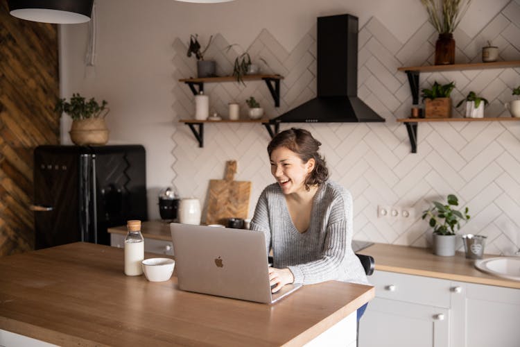 Happy Woman Using Laptop In Kitchen