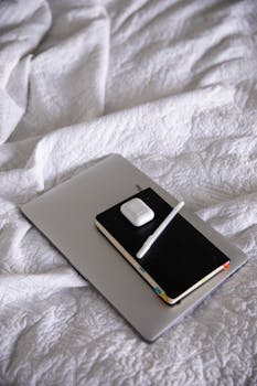 A comfortable home workspace setup featuring a laptop, notebook, and pen on a bed, ideal for remote work.