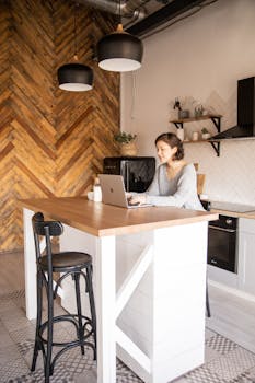 A young woman freelancing on her laptop in a stylish, modern kitchen setting, embracing remote work.