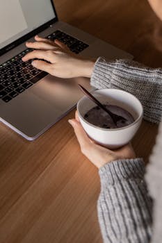 人在室内用一台笔记本电脑工作，同时吃着一碗早餐