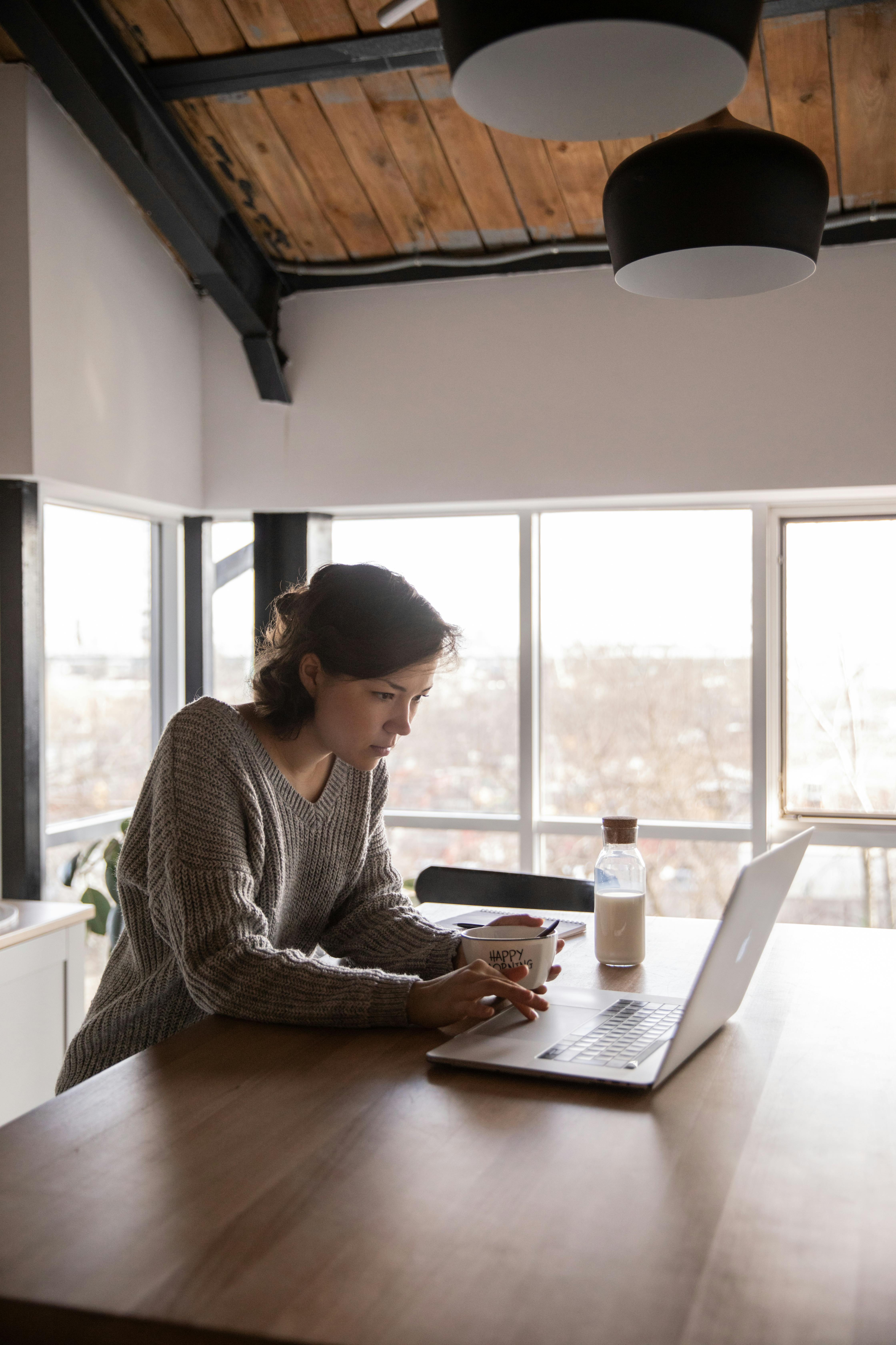 focused young woman using laptop in kitchen during breakfast