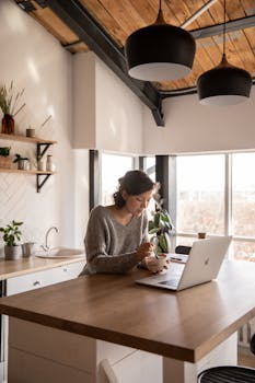 Young woman enjoying breakfast while working remotely in a cozy kitchen setting.