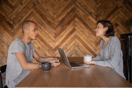 Two diverse adults discussing a project in a cozy workspace over coffee with a laptop.