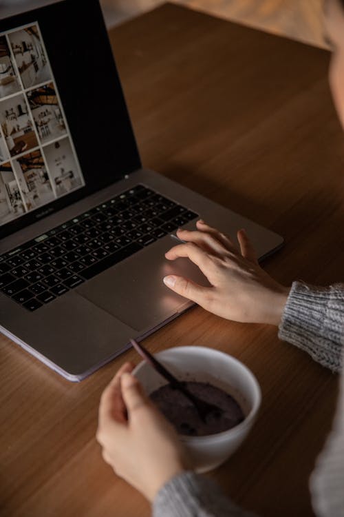 Crop young woman using laptop and eating breakfast