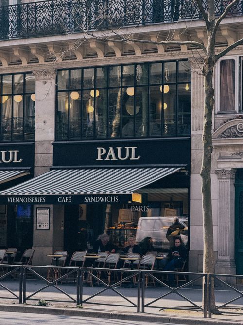 Free Street view of a classic Parisian cafe with patrons enjoying outdoor seating. Stock Photo