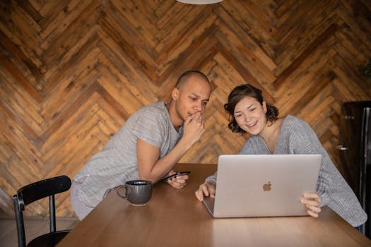 Cheerful couple smiling while using a laptop at home.