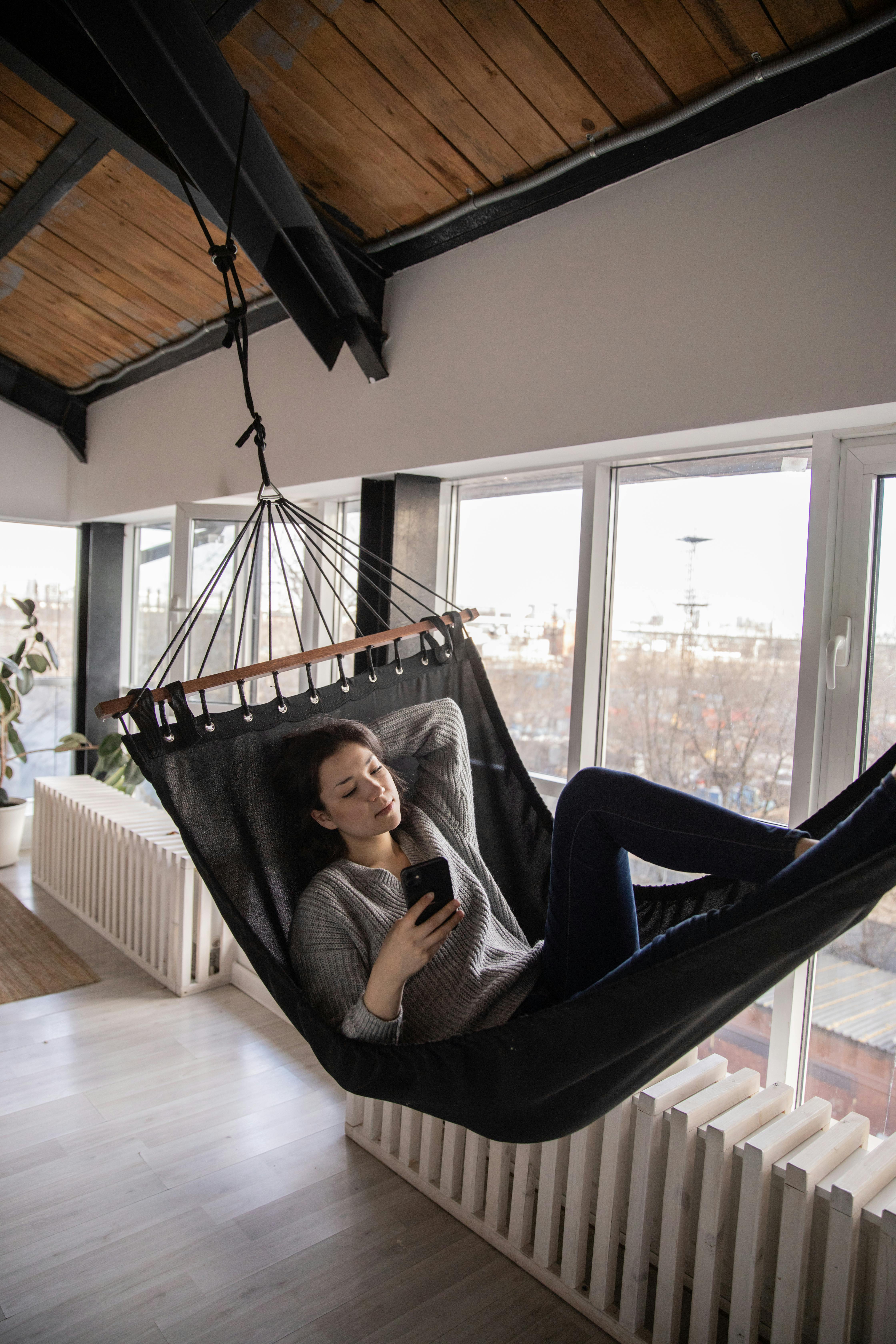pensive woman using smartphone while lying in hammock