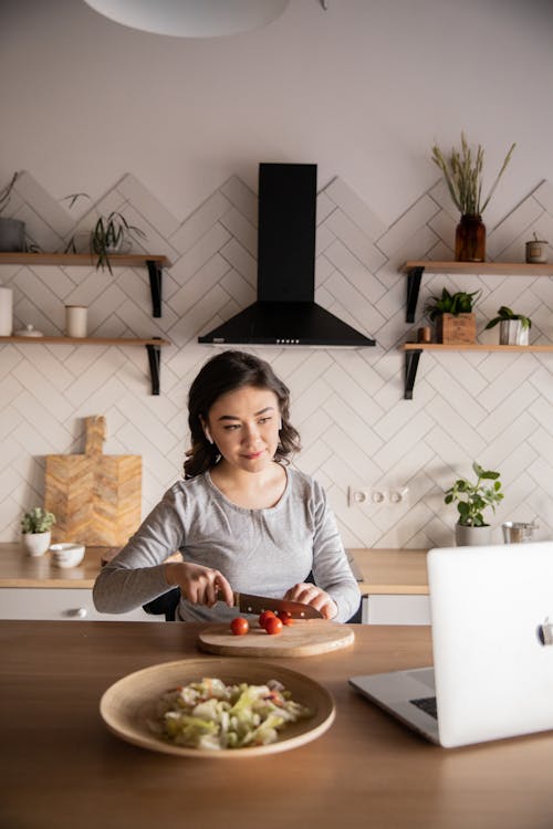 Young woman cooking while watching video on laptop