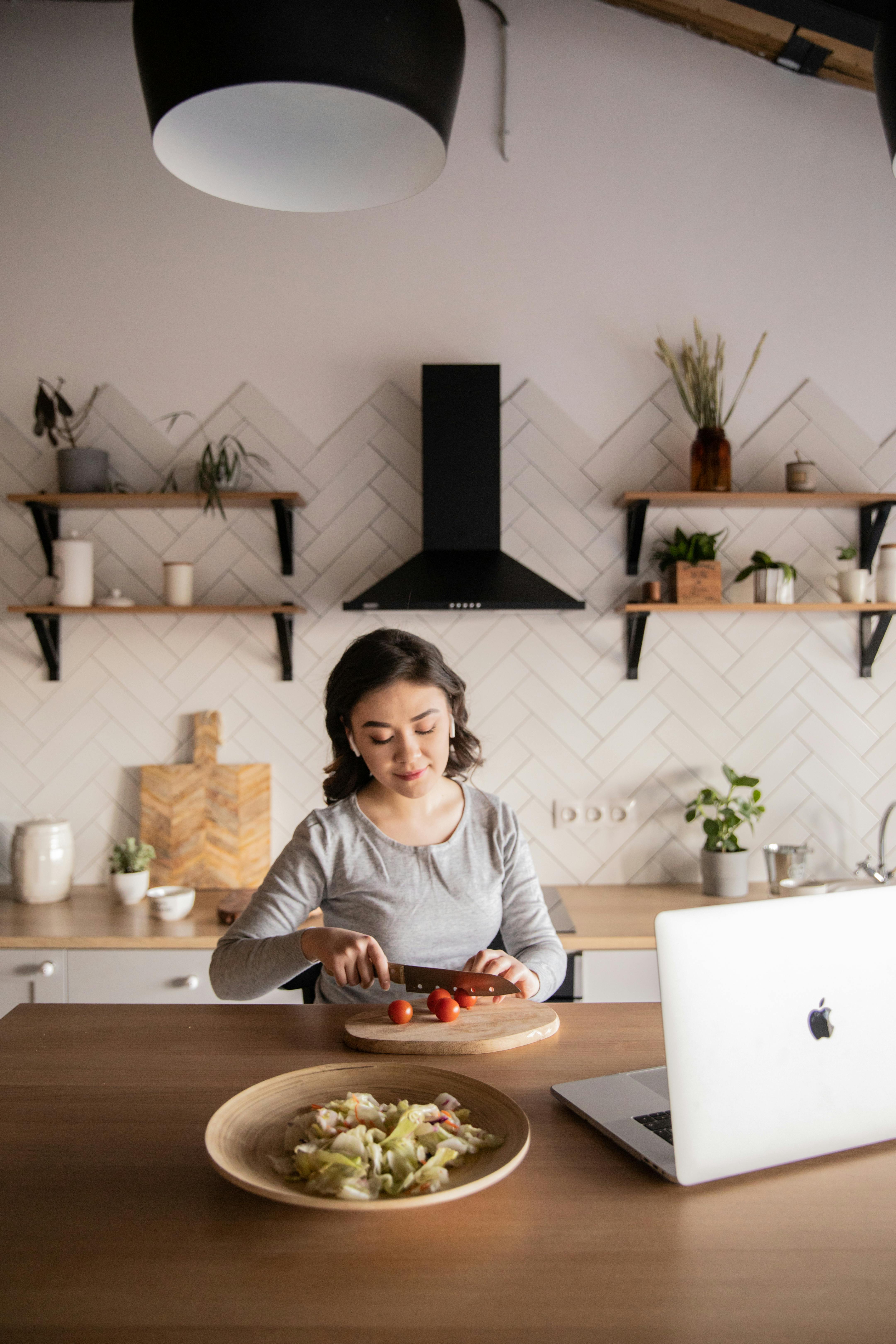 young woman preparing salad while watching video on laptop