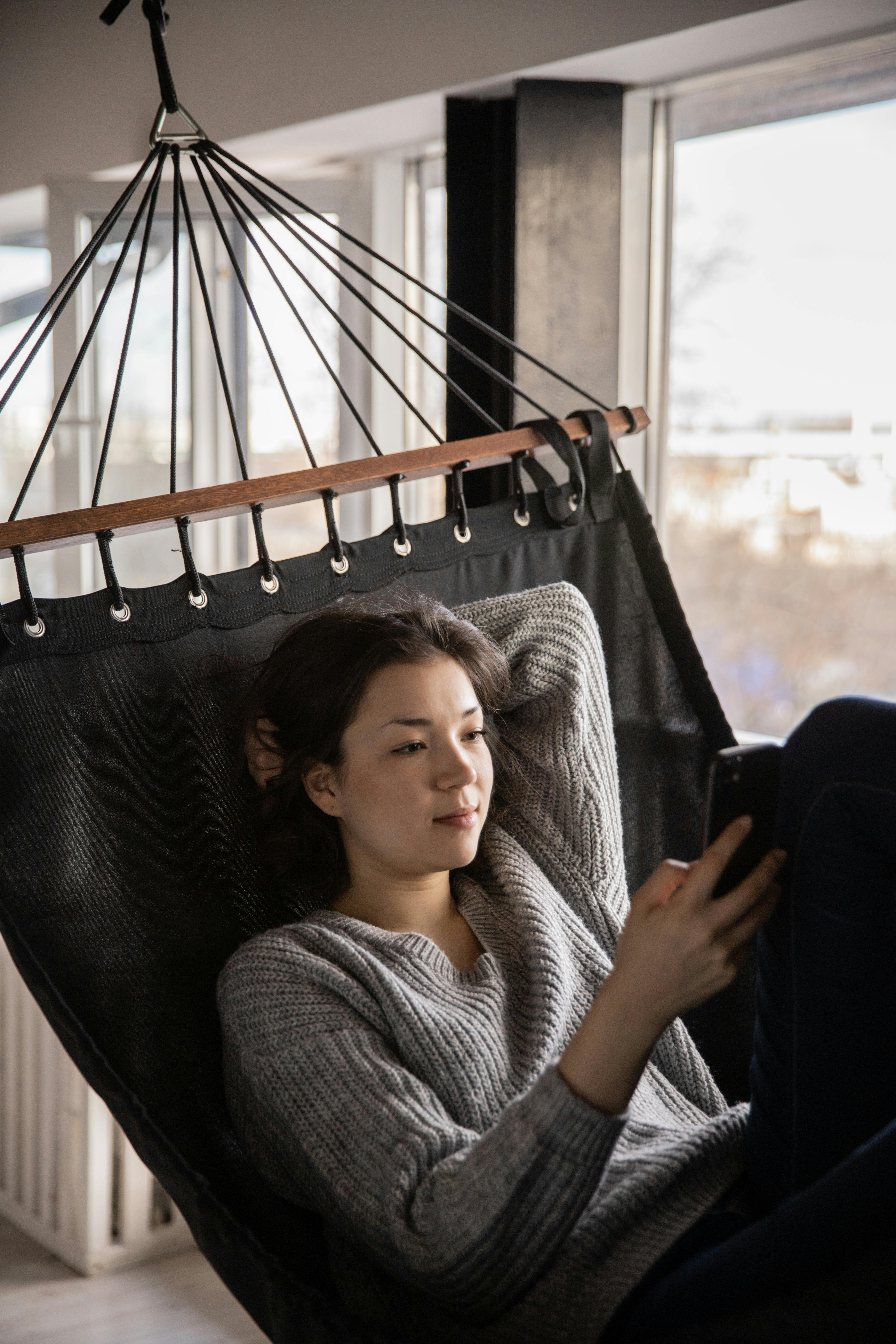 calm woman chatting on smartphone lying in hammock at home