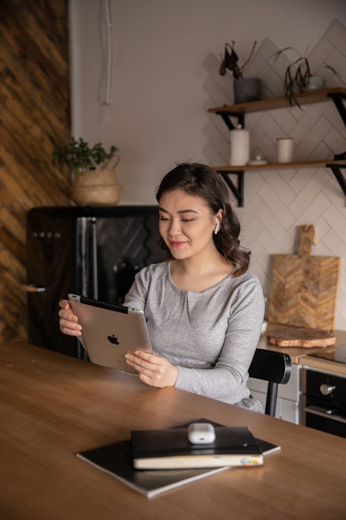 Happy ethnic woman watching tablet at table in kitchen