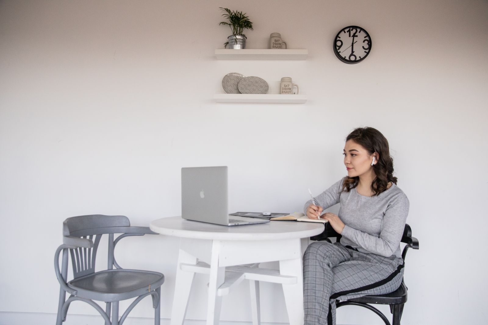 Student with wireless earbuds using a laptop while writing study notes in a notebook, combining visual and listening activities