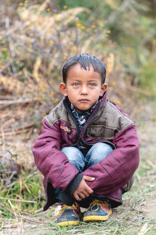 Little boy sitting on ground near greenery