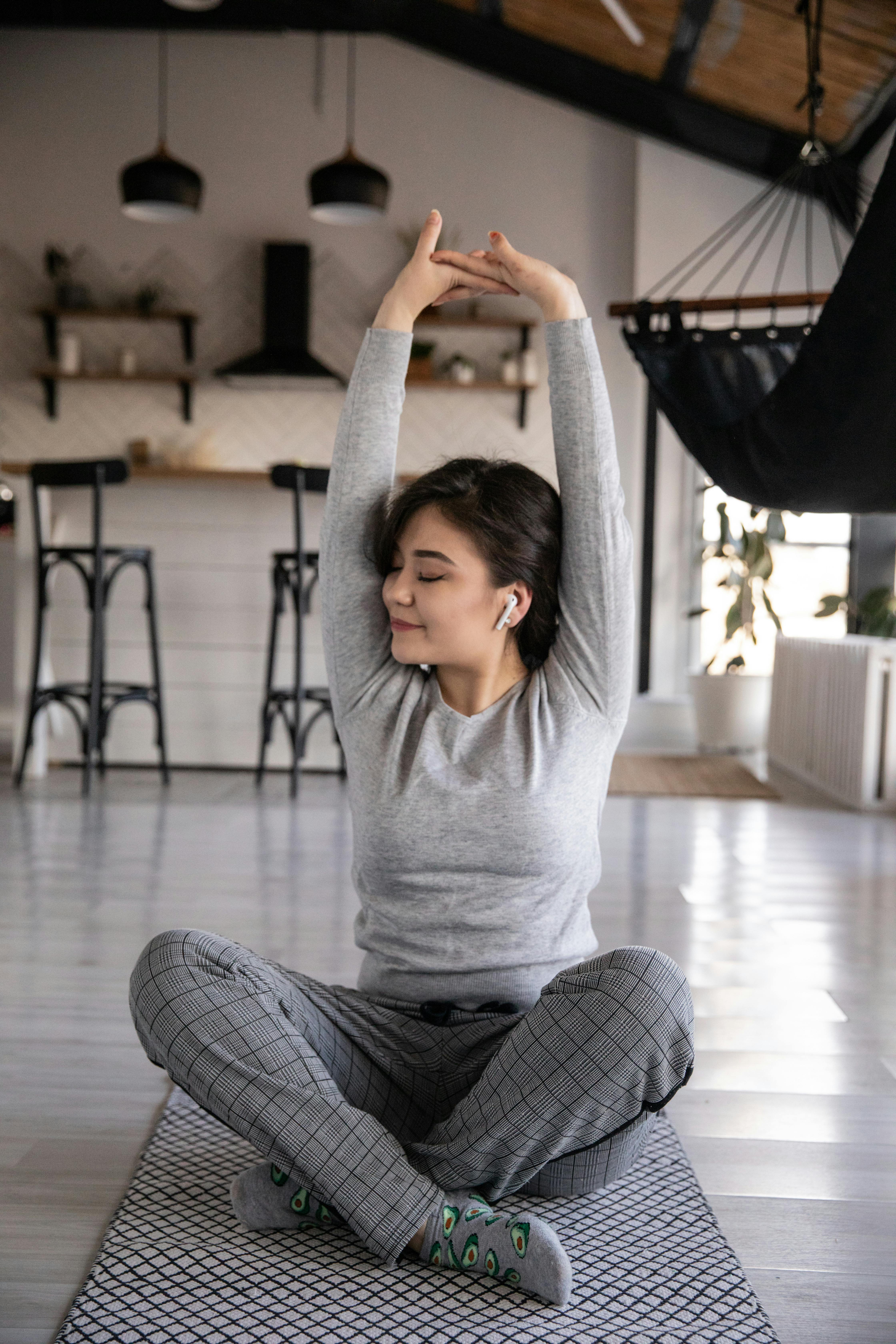 ethnic woman in earbuds sitting in lotus pose at home