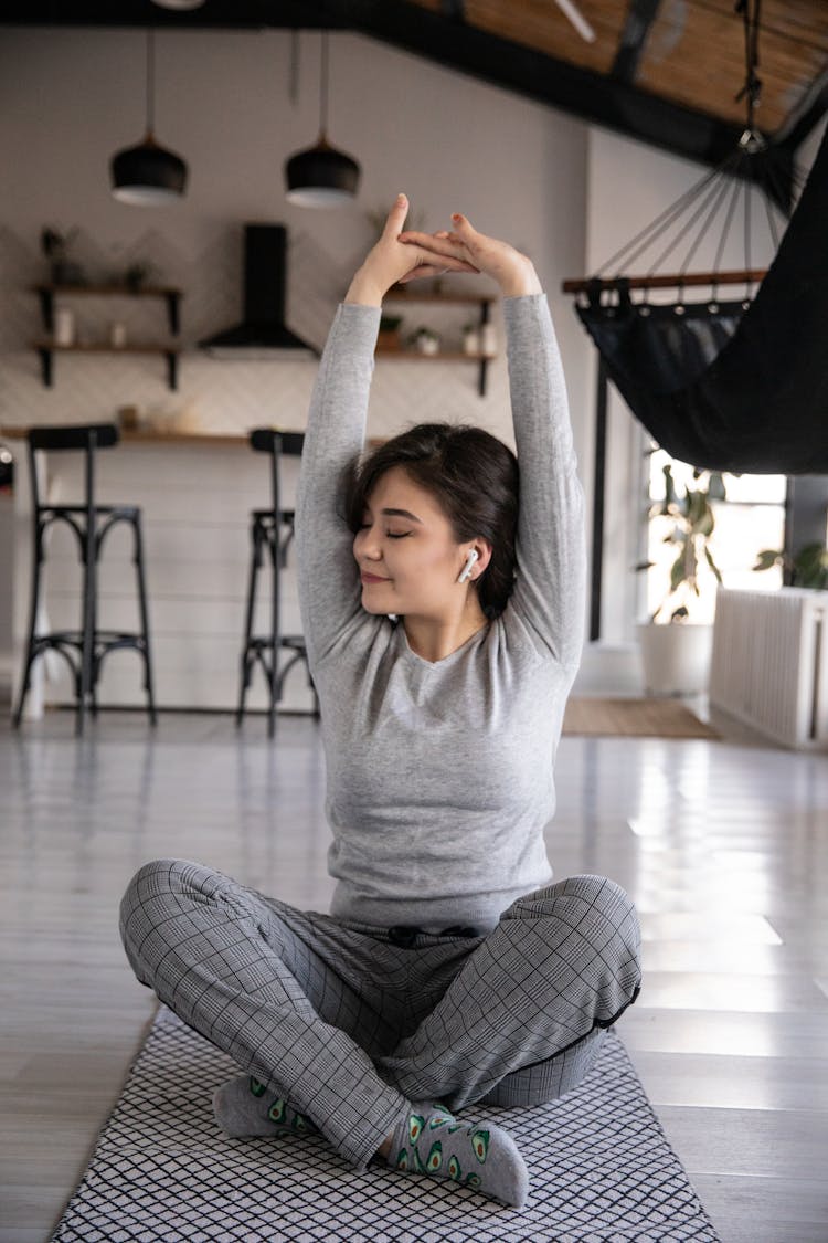 Ethnic Woman In Earbuds Sitting In Lotus Pose At Home