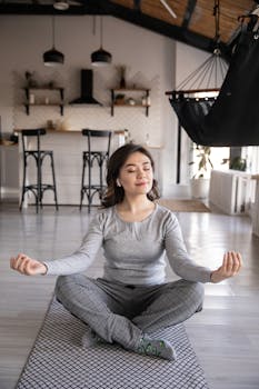 A woman meditates peacefully on a yoga mat indoors, promoting mindfulness and relaxation.