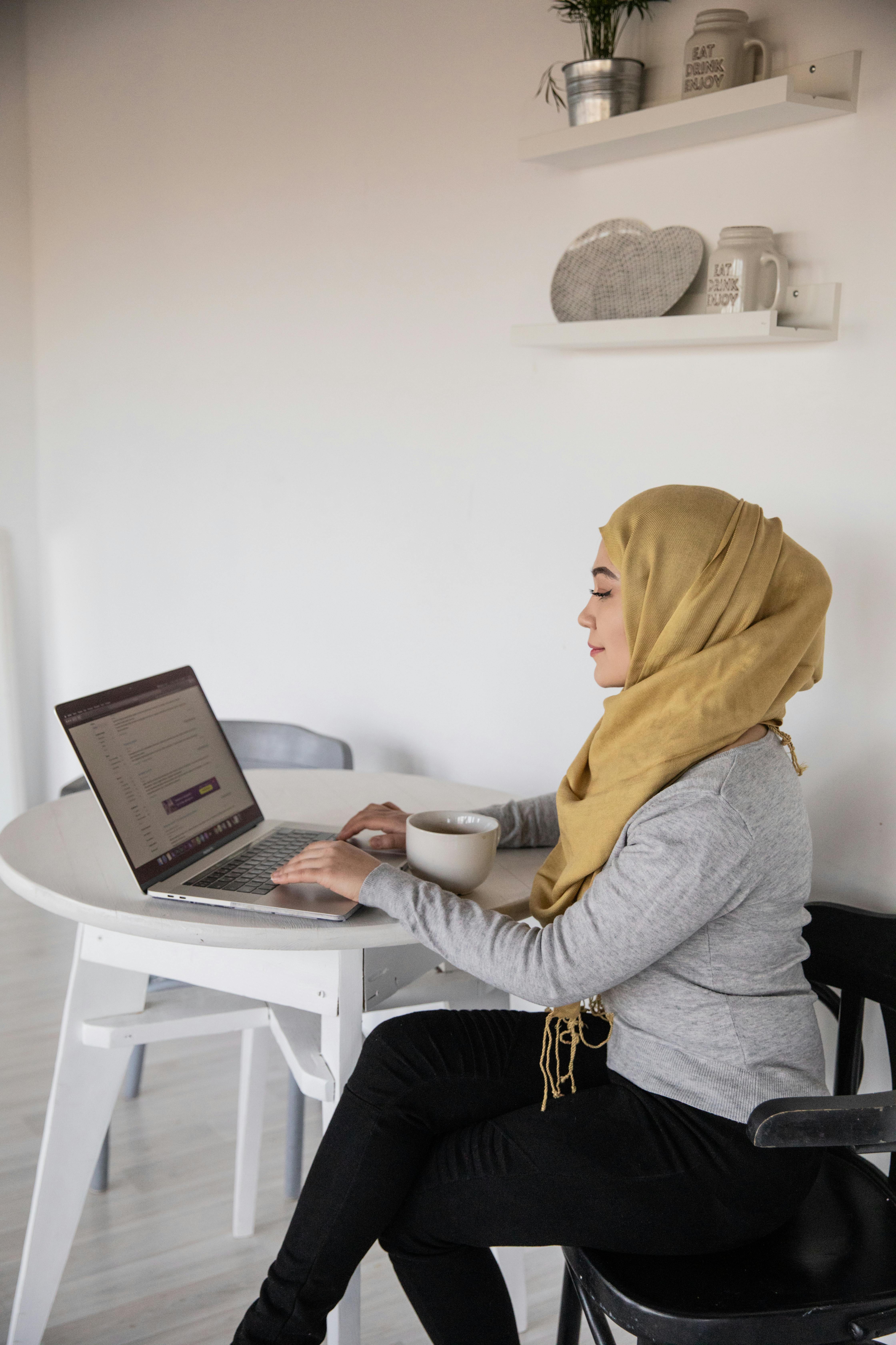 muslim businesswoman typing on laptop during coffee break at home