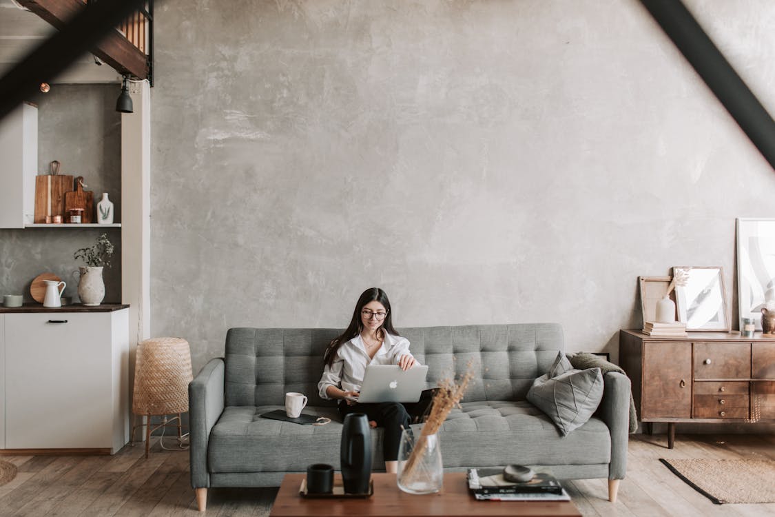 Happy female remote worker in eyeglasses sitting on cozy sofa with netbook | Photo by Vlada Karpovich from Pexels