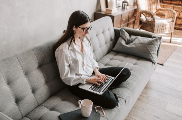 A person working comfortably on a laptop by a bright window at home