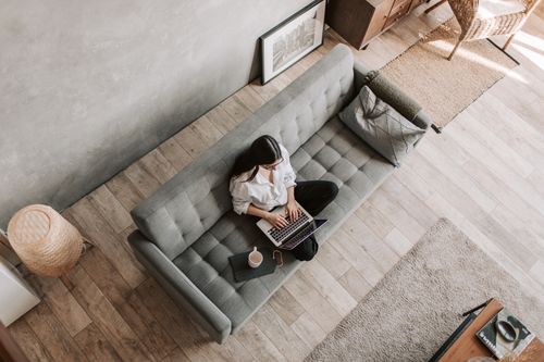 Free High angle view of a woman working on a laptop while sitting on a sofa in a modern living room. Stock Photo