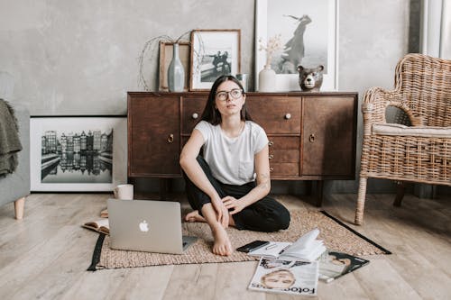 Free Pensive young lady sitting on rug in modern apartment Stock Photo