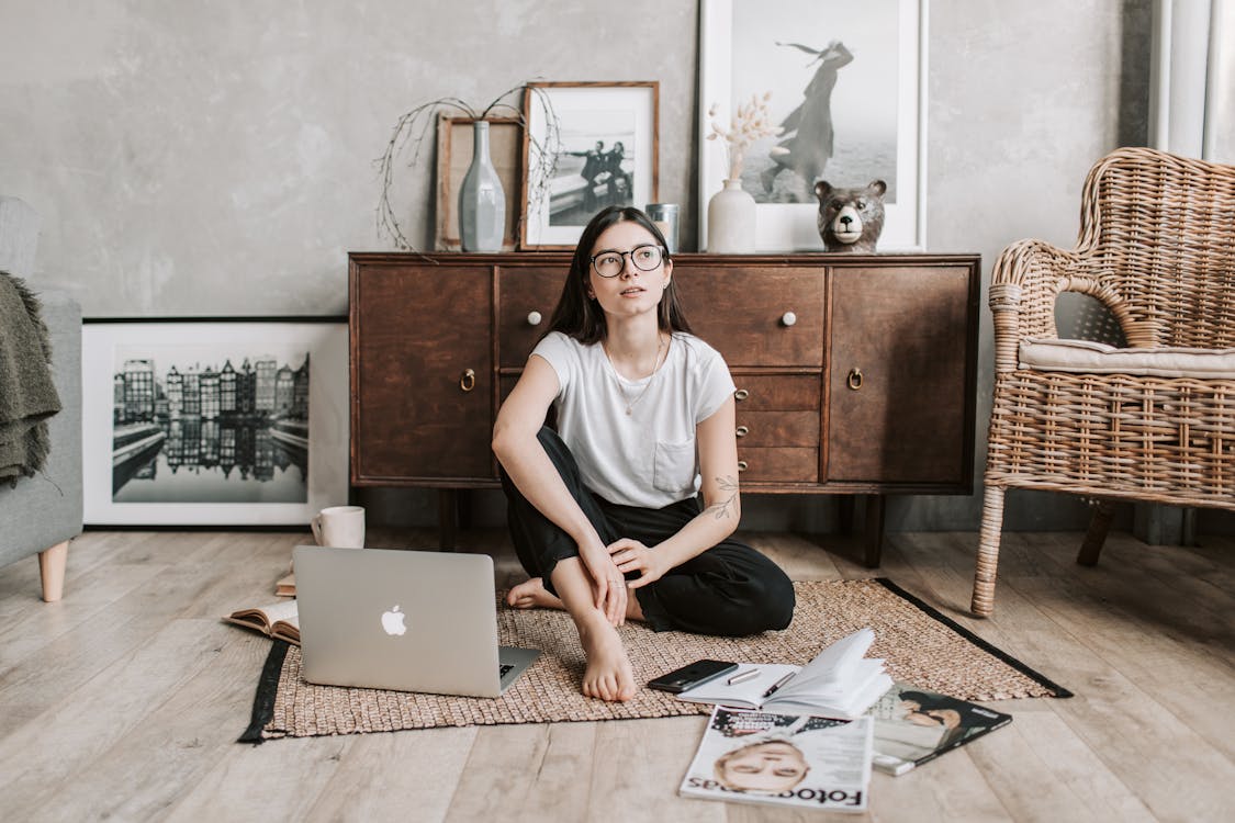 Free Pensive young lady sitting on rug in modern apartment Stock Photo