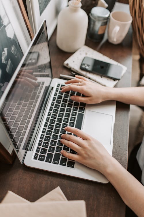 Free From above of unrecognizable woman sitting at table and typing on keyboard of computer during remote work in modern workspace Stock Photo