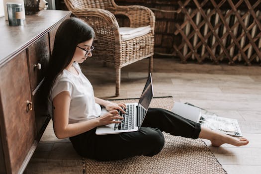 Woman at home working remotely on laptop, seated on floor in a modern interior.