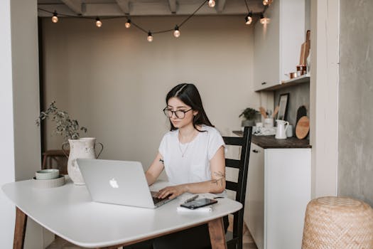 Young woman using a laptop in a stylish home office setting, focusing on remote work tasks.