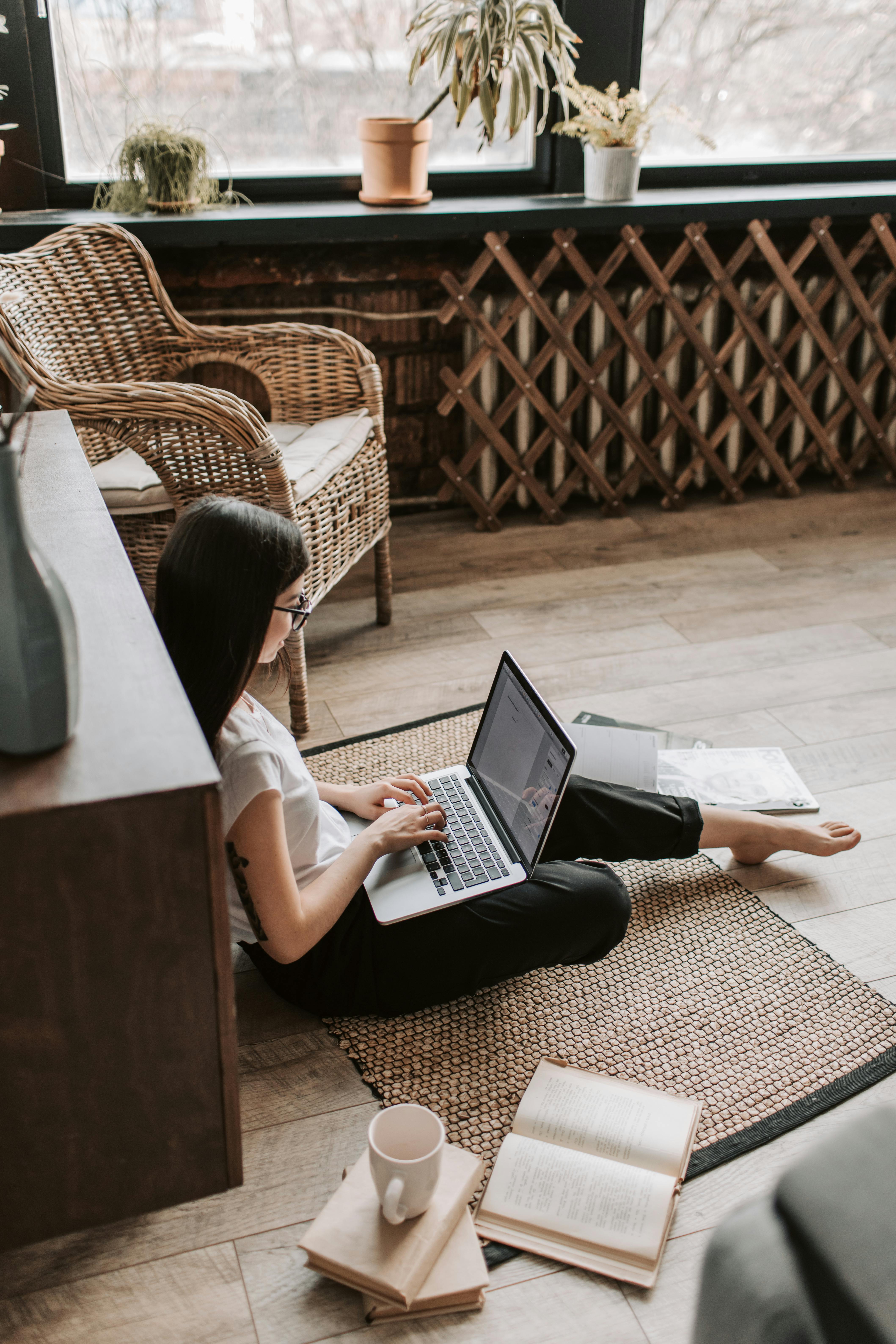 young barefoot woman using laptop on floor near books in stylish living room